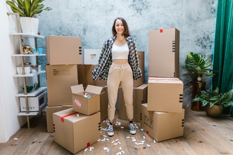 The ultimate guide to moving alone and thriving A girl standing near cardboard boxes and smiling.