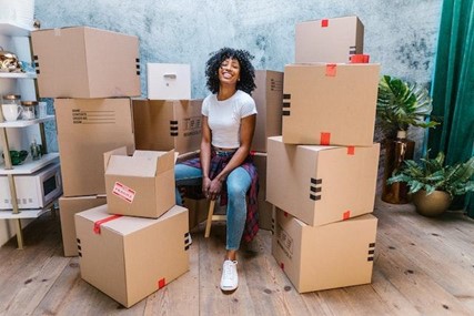 HOW MOVING TO A NEW PLACE CAN BENEFIT YOUR MENTAL HEALTH A woman sitting next to cardboard boxes.